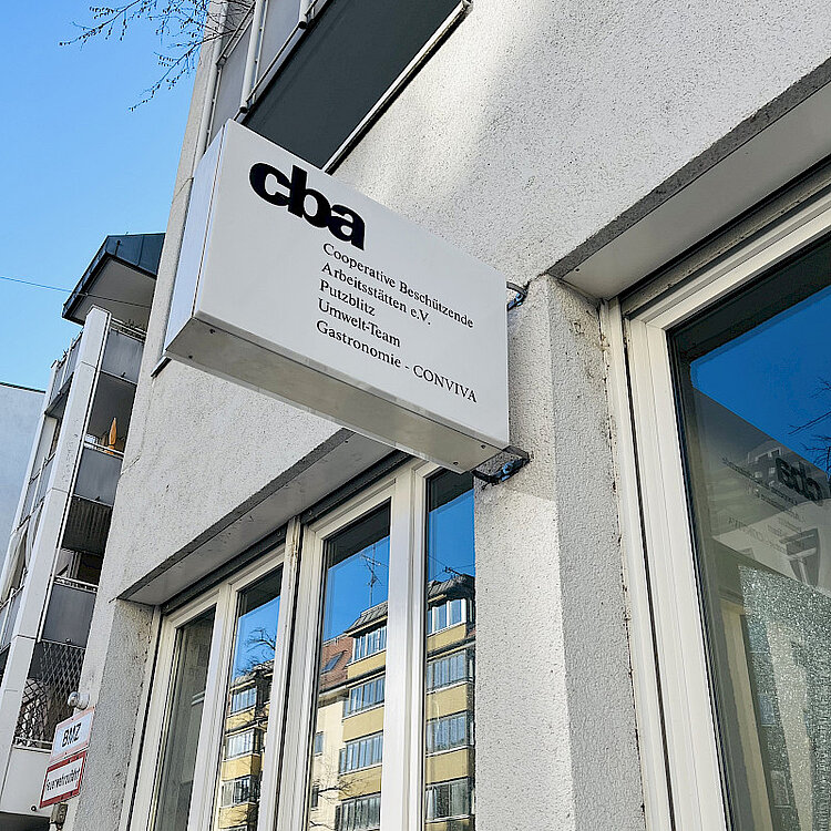 Außenaufnahme eines Gebäudes mit einem Schild, auf dem „cba Cooperative Beschäftigende Arbeitsstätten e.V. Publizistik Umwelt-Team Gastronomie CONVIVA“ steht.