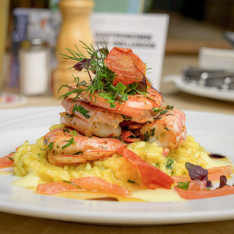 Ein Teller mit cremigem Risotto, darauf mehrere gegrillte Garnelen, garniert mit frischen Kräutern und roten Gemüsestücken.